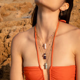 Model wearing Orange bathing suit with three ASSYA Astra Crystal necklaces layered with rocky background